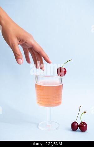 Mano femminile toccare un bicchiere di limonata rosa. Concetto di bevanda estiva. Vita creativa di rinfrescante limonata di bacche e ciliegie. Foto Stock