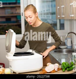 Donna sorridente che cucina con multicooker elettrico a casa cucina Foto Stock