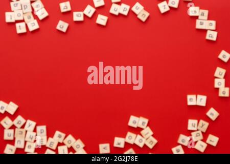 Immagine di sfondo le lettere sono sparse in disordine. Lettere inglesi. Lettere quadrate di legno su sfondo rosso brillante. Biglietto d'auguri, pronto all'uso Foto Stock