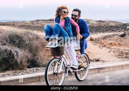 Giovane coppia che si diverte in attività di svago all'aperto insieme - giovane coppia che va per un giro in bicicletta in un giorno d'autunno in città - uomo portare donna e sia ridere e godere di stile di vita e amore Foto Stock