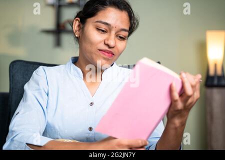 Felice giovane donna d'affari leggere libro o studiare durante il tempo libero o per l'esame a casa da seduta sul divano a casa - concetto di lettura Foto Stock