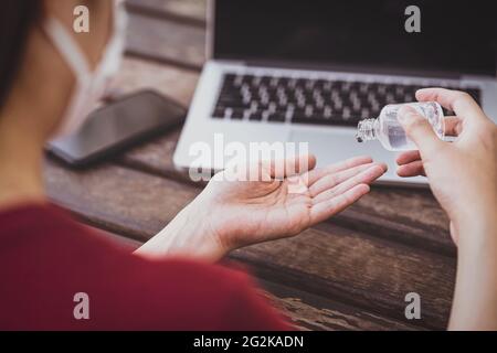 Vista posteriore di una donna asiatica che fa disinfettante mani pompando gel di alcol prima di lavorare con la tecnologia laptop, lavorando da casa in Covid-19 pandemia, socia Foto Stock