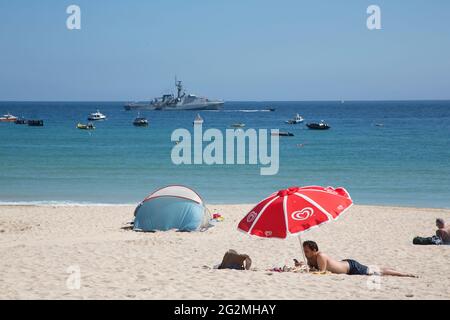 St Ives, Regno Unito. 12 giugno 2021. Il sole finalmente esce il secondo giorno del vertice dei leader del G7 in Cornovaglia. I bagnanti si trovano sulla spiaggia di Porthminster, mentre un cacciatorpediniere pattugge la baia. Credit: Sarah Peters/Alamy Live News Foto Stock