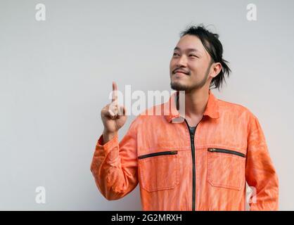 Il capo meccanico in una uniforme arancione che punta un dito verso l'alto. Ritratto su sfondo grigio con luce da studio. Foto Stock