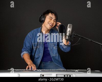 Giovane asiatico con cuffie che suonano una tastiera elettrica davanti alle  pareti nere insonorizzate. Musicisti che producono musica in recordin  professionale Foto stock - Alamy