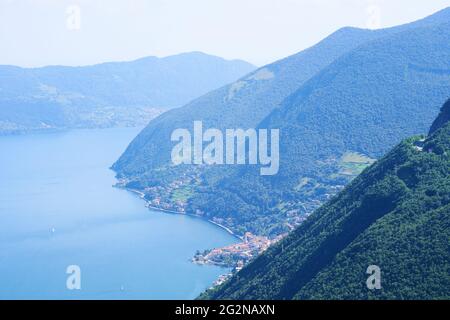 Pittoresco paesaggio estivo. Vista aerea del lago d'Iseo, montagne boscose, vari villaggi sparsi lungo le pendici delle montagne e lungo la costa. Foto Stock