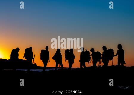 Silhouette al tramonto: Un gruppo di avventurieri percorre l'orizzonte, i loro zaini incisi su un cielo vibrante, incarnando lo spirito di esplorazione Foto Stock