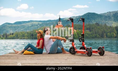 Giovane coppia che usa lo scooter elettrico come moderno mezzo di trasporto ecologico mentre esplora il verde paese Slovenia in vacanza. Energia ecologica verde Foto Stock