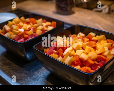 Frutta fresca tagliata in una ciotola nera al tavolo del buffet. Fuoco selettivo sui frutti. Foto Stock