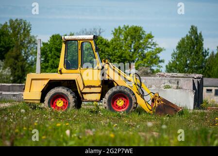 Escavatore giallo con dischi rossi su un'erba verde contro il cielo blu Foto Stock