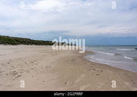 Una bella spiaggia di sabbia bianca con un faro sullo sfondo in alto su dune di sabbia erbosa Foto Stock