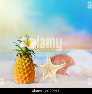 Ananas con fiore e conchiglia in spiaggia. Concetto estivo. Foto Stock