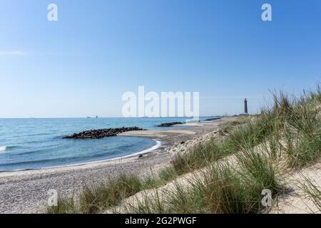 Una bella spiaggia vuota dietro le dune di sabbia con tempeste rocciose per proteggere dall'erosione e il faro Skagen sullo sfondo Foto Stock