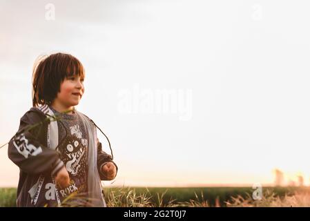 Ritratto di un ragazzino su un prato verde che guarda il tramonto godendo la natura estate sera all'aperto Foto Stock