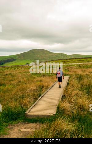 Uomo che cammina su tavole d'anatra verso la mini montagna Cheshire Shutlingsloe nel quartiere White Peak Foto Stock