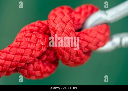Un primo piano di una corda di nylon rosso legata in un nodo ad un gancio di metallo Foto Stock