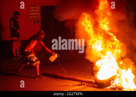 Un dimostratore getta benzina ad un fuoco attivo mentre la gente si scontra con la polizia di rivolta della Colombia (ESMAD) sulla strada che collega Cartago, Valle del Cauca con la città di Pereira, Risaralda, Colombia 11 giugno 2021. Foto Stock