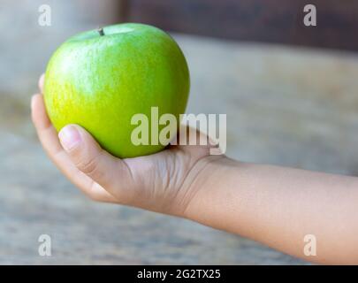 Il bambino tiene una mela verde su uno sfondo di legno Foto Stock