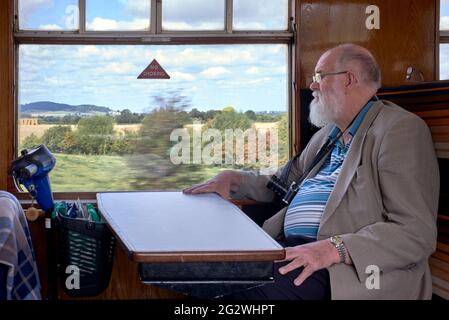 Il treno senior viaggia con i cittadini a bordo del treno a vapore GWR d'epoca che viaggia attraverso la campagna inglese. Inghilterra Regno Unito. Foto Stock