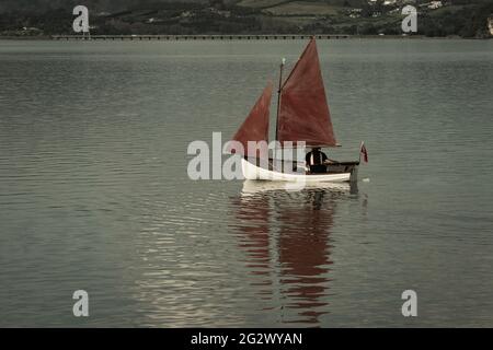 Vele rosse in stile vintage tradizionale su un piccolo yacht attratti nella baia. Foto Stock