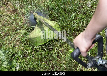 Un uomo con un rasaerba elettrico taglia l'erba. Per un negozio di attrezzature da giardinaggio. Foto Stock