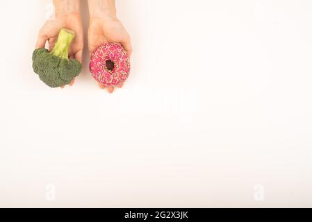 Confronto delle abitudini alimentari. Donna che tiene broccoli e ciambella su sfondo bianco. Spazio di copia Foto Stock