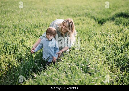 La giovane madre gioca con il suo figlio di 3 anni su campo d'erba, l'erba verde è quasi alto come il ragazzo. Felice concetto di maternità Foto Stock