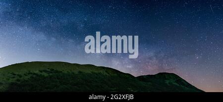 Cielo notturno panoramico sugli altipiani di Montelago, Marche, Italia. L'arco galassico della Via Lattea e le stelle che si innalzano da un paesaggio unico di colline verdi. Foto Stock