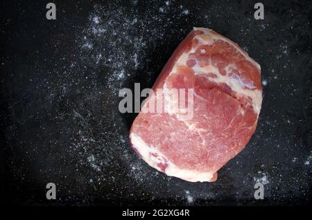 Pezzo di maiale crudo con sale su fondo nero. Vista dall'alto di un pezzo di maiale disossato fresco. Pezzo di carne grande. Cibo e cucina concetto. Foto Stock