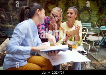 tre giovani donne caucasiche adulte studiano insieme in un caffè all'aperto, divertendosi Foto Stock