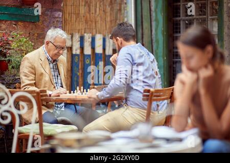 uomo giovane e anziano che gioca a scacchi in un caffè all'aperto, pensando. immagine di messa a fuoco selettiva Foto Stock