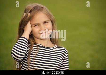 Sorriso felice piccolo capretto che corre le dita attraverso lunghi capelli biondi paesaggio naturale estivo, cura dei capelli, spazio di copia Foto Stock