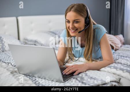 Bella donna con le cuffie ama usare il computer portatile in camera da letto . Foto Stock