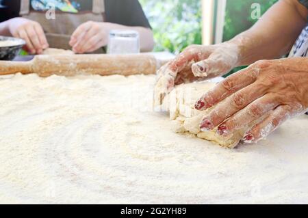 Il cuoco insegna ai bambini a fare l'impasto. La mano femminile impasta l'impasto su un tavolo infarinato. Master class in cottura. Cucinare a casa. Spazio di copia Foto Stock