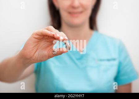 Apparecchi acustici, trattamento di sordità. Primo piano di un audiologo che tiene in mano un moderno apparecchio acustico Foto Stock