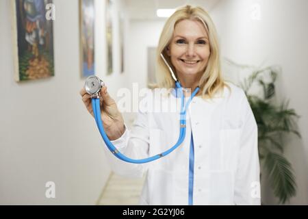 occupazione medica. Medico di medicina generale con esperienza che indossa un cappotto medico con stetoscopio in mano, in piedi in una clinica medica, ritratto Foto Stock