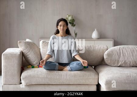 Calma donna ispanica pratica yoga seduta sul divano Foto Stock