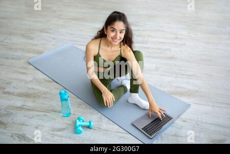 Giovane donna indiana che guarda online tutorial sportivo sul laptop prima di allenarsi a casa. Stile di vita attivo Foto Stock