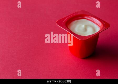 Tazza di yogurt su sfondo rosso - delizioso yogurt di frutta in pentola di plastica rossa con spazio per la copia Foto Stock