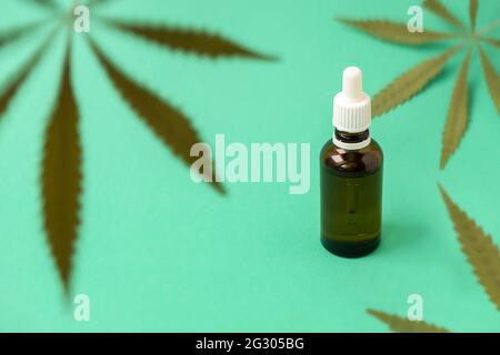 Foglie verdi di marijuana su sfondo verde con olio di cannabis in una bottiglia di vetro, fuoco selettivo. Concetto di cannabis per scopi medicinali Foto Stock
