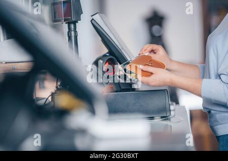 Processo di scansione del codice a barre su una merce in un negozio, venditore che vende una borsa a un cliente Foto Stock