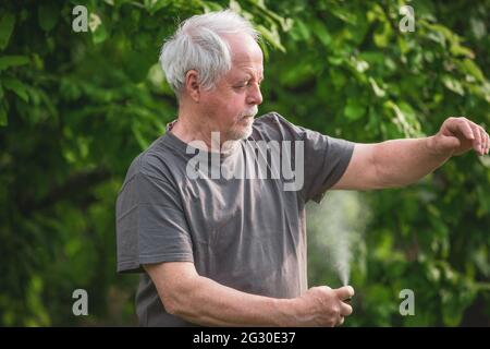 L'uomo anziano spruzzando o usando repellente contro genere di insetti, zanzare e zecche nella foresta, spray protettivo, concetto di sanità Foto Stock