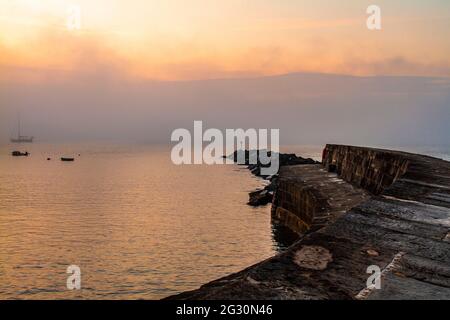 Un cielo arancione sopra la parete del porto al Cobb all'alba. Lyme Regis, Dorset, Regno Unito. Scena della donna tenente francese. Spazio di copia Foto Stock