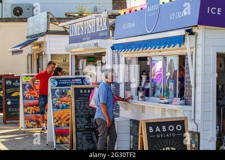 La gente coda, socialmente distanziata, per gelato e pesce & patatine, alle bancarelle da asporto sulla spiaggia di Lyme Regis, Jurassic Coast, Dorset, Inghilterra Foto Stock