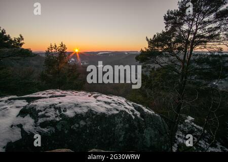 Paesaggio invernale in foresta con coppia seduta sulla panchina al tramonto in luce dorata, Mullerthal, Lussemburgo Foto Stock