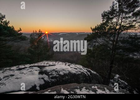 Paesaggio invernale in foresta con coppia seduta sulla panchina al tramonto in luce dorata, Mullerthal, Lussemburgo Foto Stock