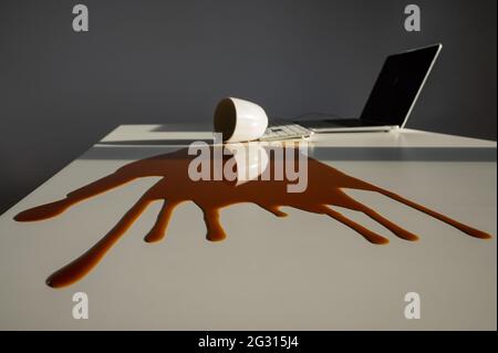 Tazza di caffè nero versato sul computer portatile su un desktop bianco. Foto Stock