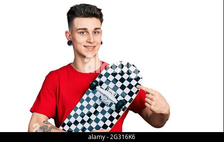 Ragazzo caucasico giovane con le orecchie dilatazione tenendo il pattino sorridendo felice puntando con mano e dito Foto Stock