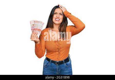 Bella donna ispanica in possesso di 10 pesos colombiani banconote stressato e frustrato con la mano sulla testa, sorpresa e faccia arrabbiata Foto Stock