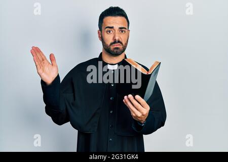 Bell'uomo prete ispanico con barba che tiene la bibbia e croce cristiana  scettica e nervosa, sconvolto a causa del problema. Persona negativa Foto  stock - Alamy